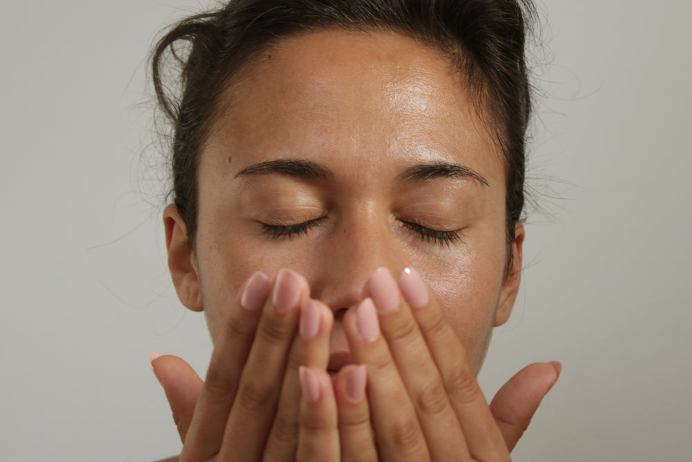 A woman holds her hands in front of her face with her eyes closed and inhales