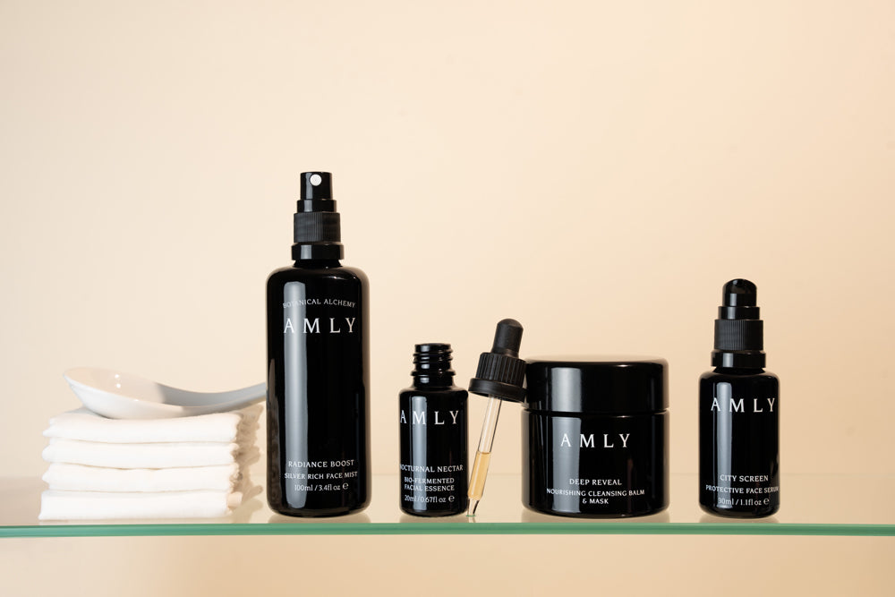 Amly products in their dark glass bottles against a cream background lined up on a glass shelf next to a pile of muslin cloths.