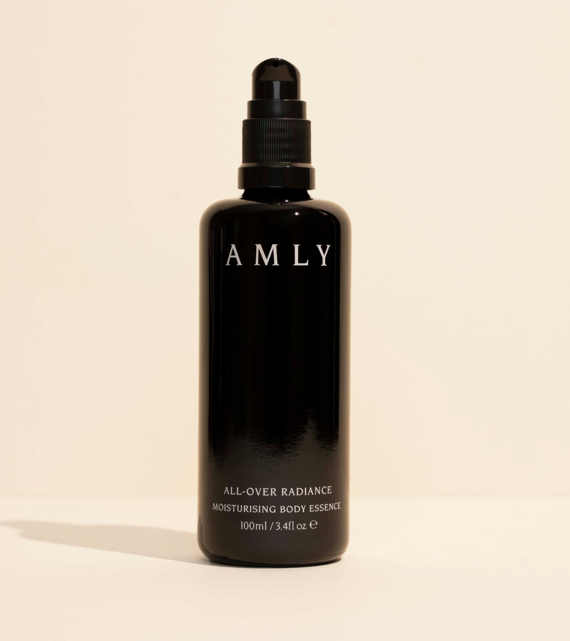 AMLY All-Over Radiance Moisturising Body Essence in a black glass pump bottle on a beige background